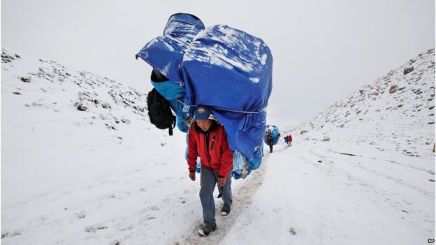 Um porteiro anda com uma carga maciça para o acampamento base de Everest